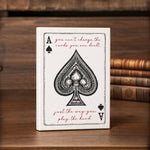 a white card with a black spade symbol and a motivational quote on it, placed on a wooden surface.