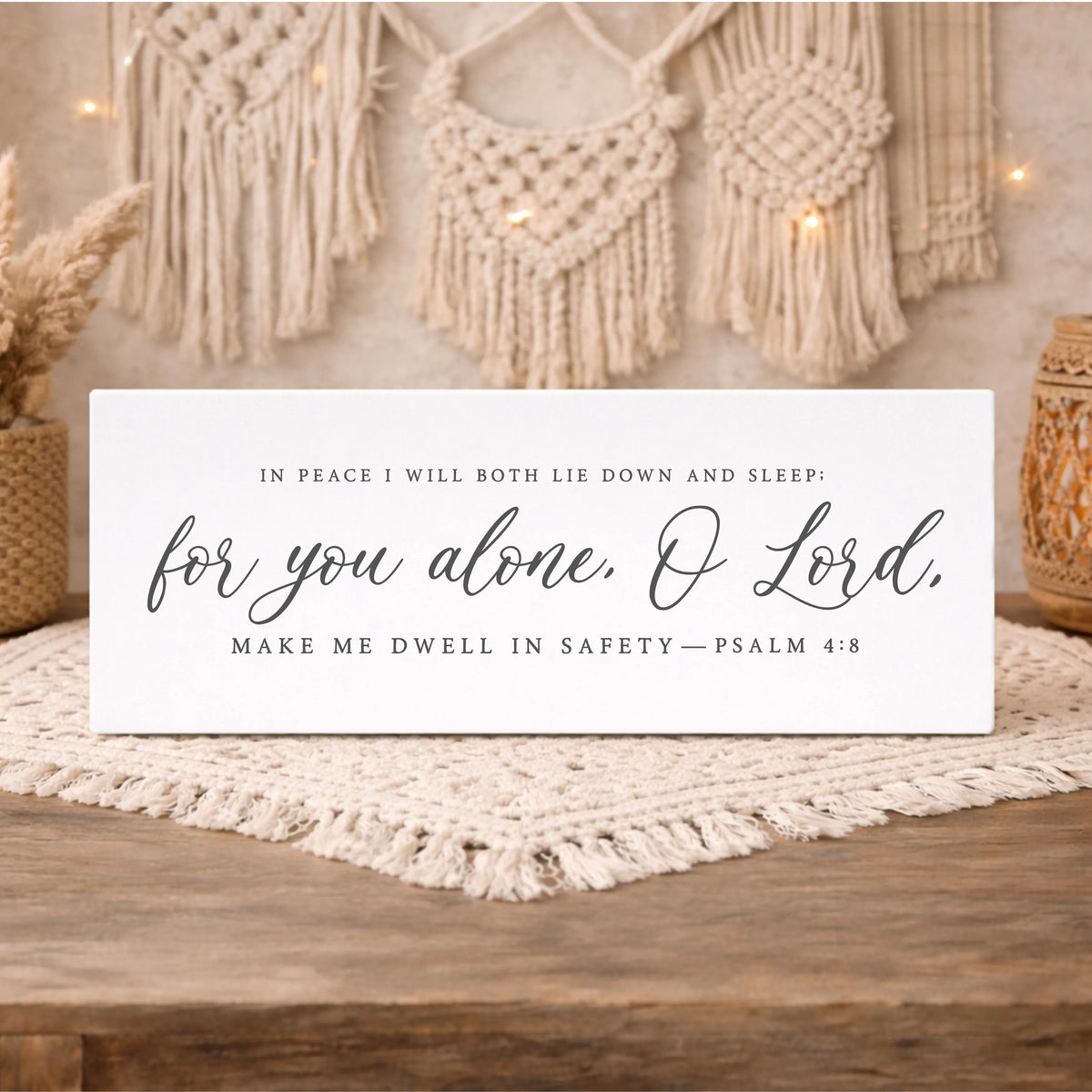 A white sign with black text that reads "In peace I will both lie down and sleep: for you alone, O Lord, Make me dwell in safety—PSALM 4:8" is displayed on a wooden surface.