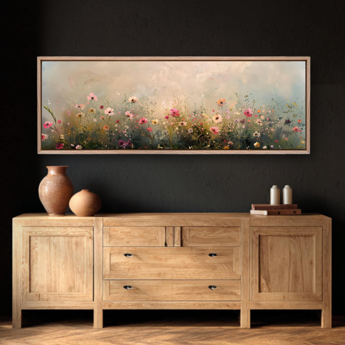 a large painting of a field of flowers hanging on a wall above a wooden cabinet with three drawers. The cabinet has a vase and some books on top of it.