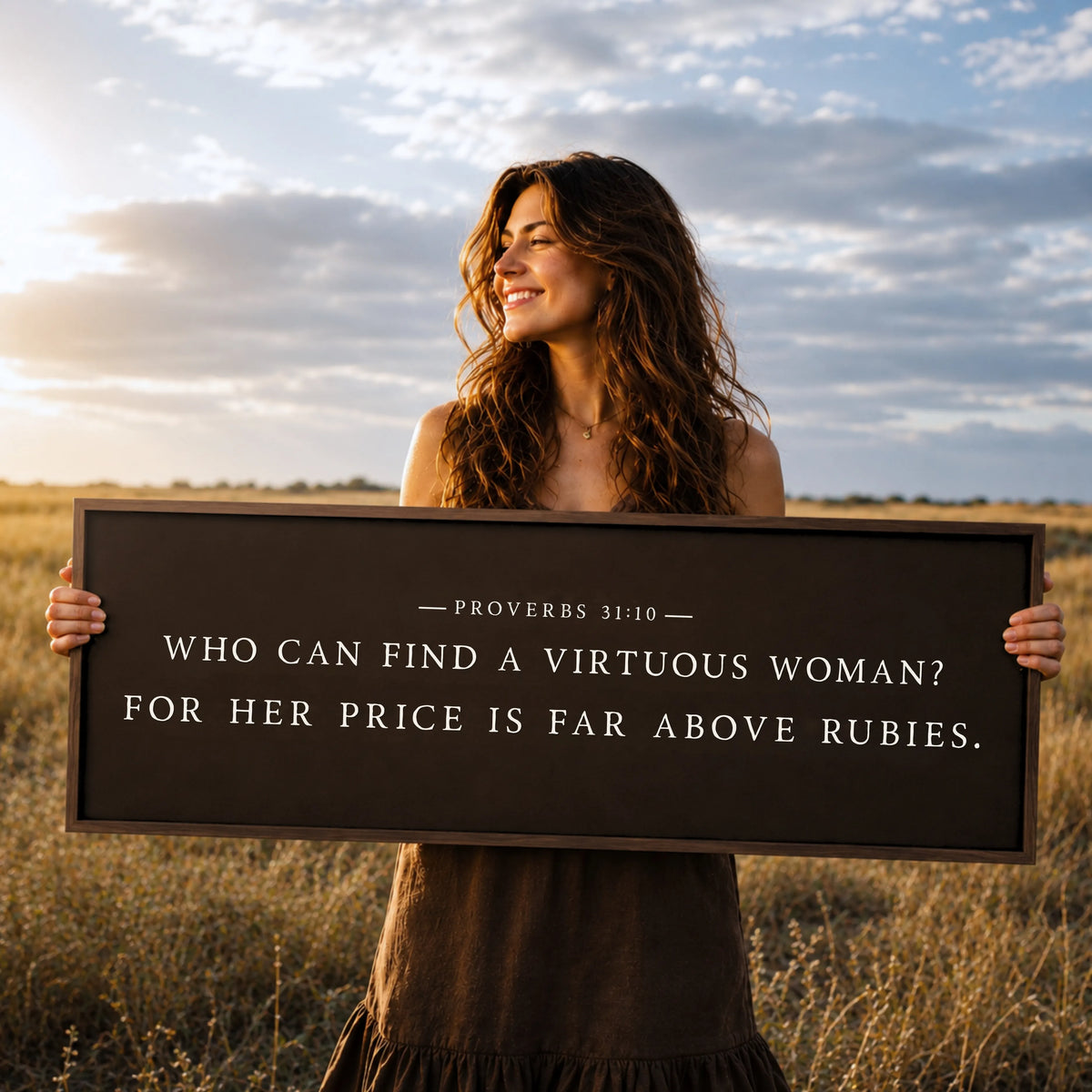 A woman stands in a field holding a sign with a Bible verse from Proverbs 31:10.