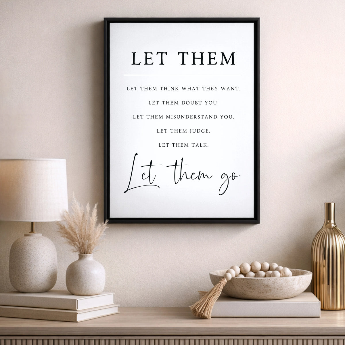 a framed quote on a wall, with a lamp, a vase with dried flowers, and a bowl of beads on a shelf below it.