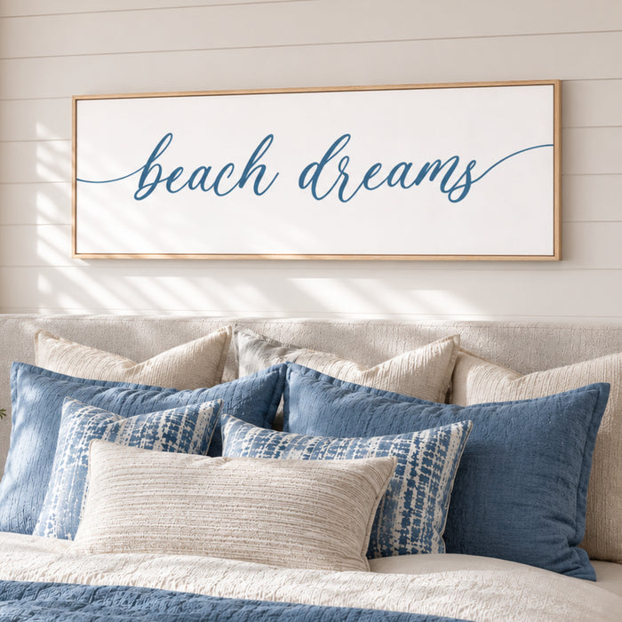 a bedroom with a bed adorned with blue and white pillows, and a framed sign above it that reads "beach dreams".