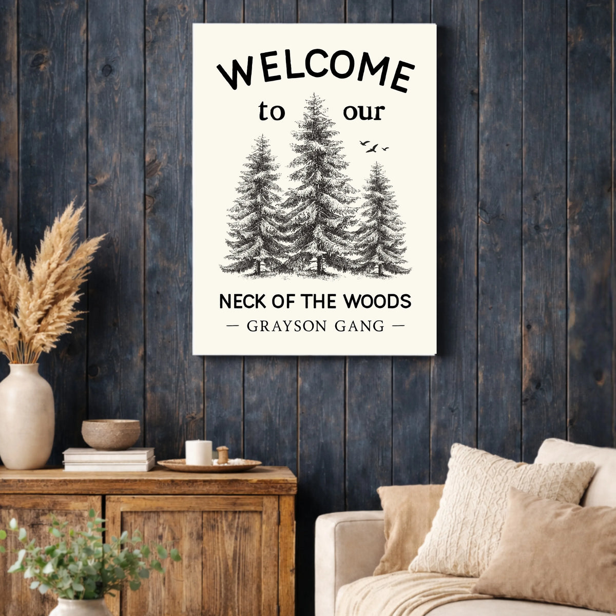 a cozy living room with a wooden cabinet, a couch, and a potted plant. Above the couch, there is a framed sign that reads "Welcome to our Neck of the Woods - Grayson Gang".