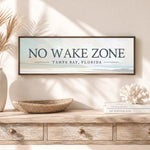 a framed sign that reads "NO WAKE ZONE" above a wooden dresser with a woven basket and a stack of books.