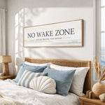 a bedroom with a large framed sign that says "NO WAKE ZONE" above a bed with white sheets and blue and white striped pillows.