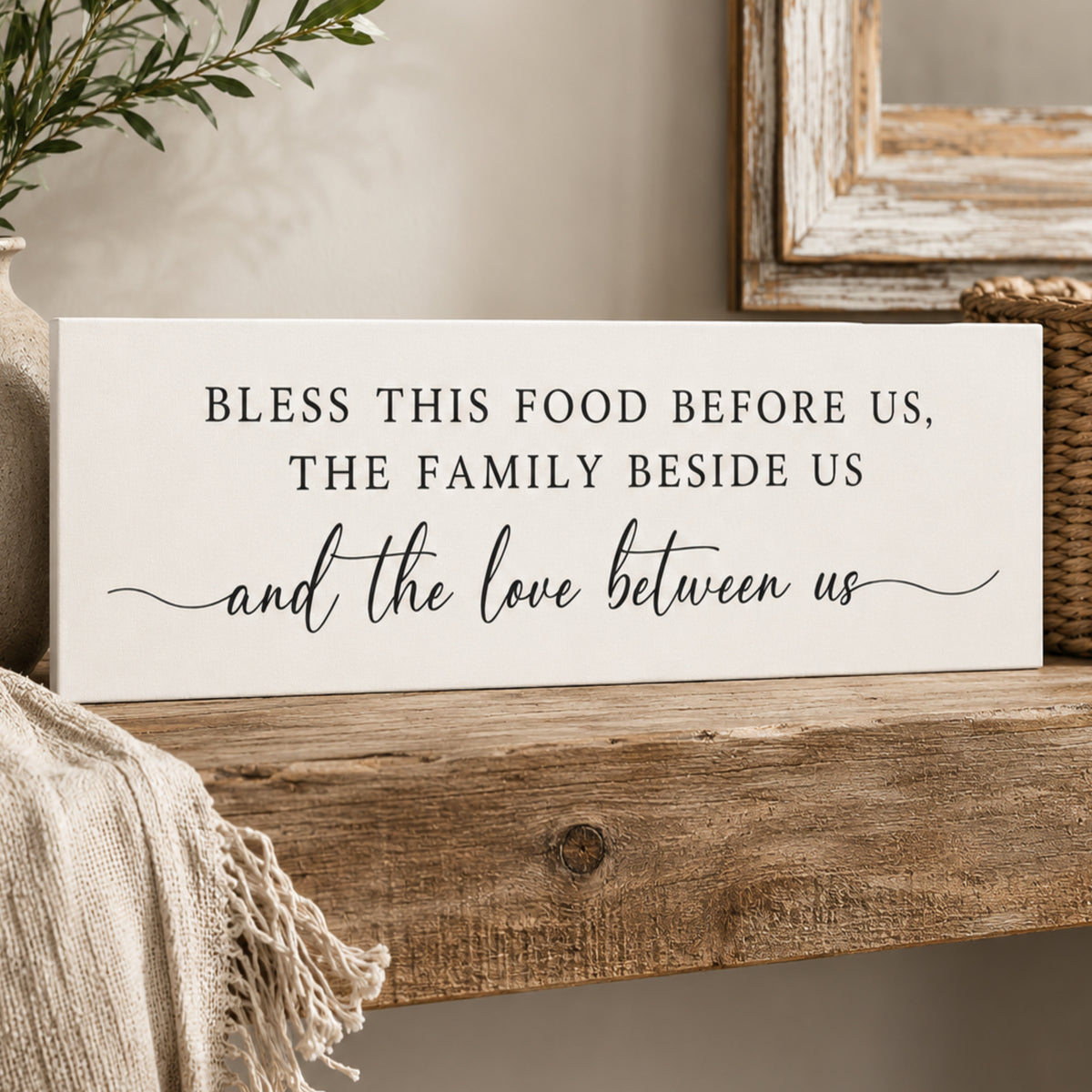 A white sign with black text that reads "Bless this food before us, the family beside us and the love between us" is displayed on a wooden shelf.