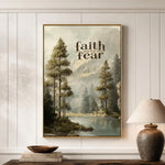 a framed painting of a serene landscape with trees, a lake, and mountains in the background, hanging on a wall above a wooden table with a lamp and a stack of books.