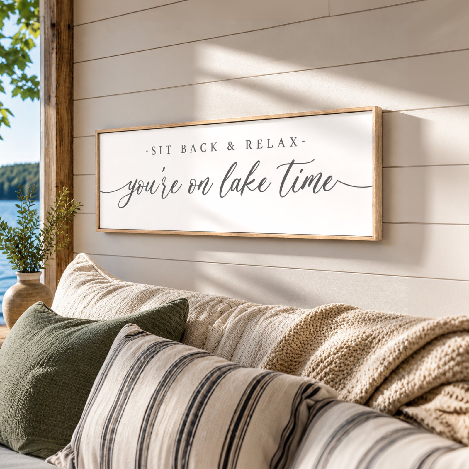 A framed sign on a wall that reads "SIT BACK & RELAX you're on lake time" with a scenic view of a lake and trees in the background.