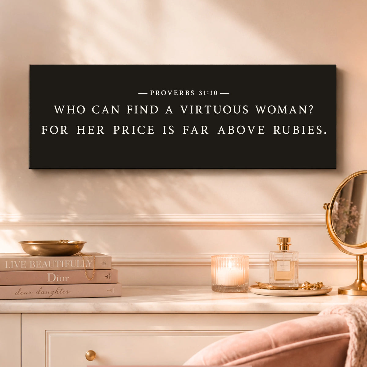 a black sign with white text that reads "WHO CAN FIND A VIRUTOUS WOMAN? FOR HER PRICE IS FAR ABOVE RUBIES." The sign is displayed on a white wall above a dresser with a mirror, a candle, and a book.