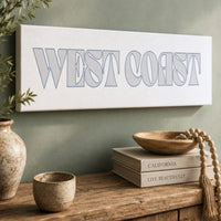 a wooden shelf with various decorative items, including a vase, a bowl, and a stack of books. Above the shelf, there is a sign that says "West Coast" in a stylized font.