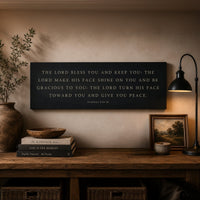 a wooden desk with a black sign displaying a Bible verse, a lamp, a plant, and some books.