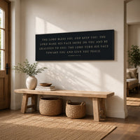 A wooden bench with woven baskets sits in a sunlit room, accompanied by a black sign with a religious message and a potted plant.